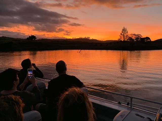 Passengers on a boat watching a vibrant orange sunset over the Daintree River.